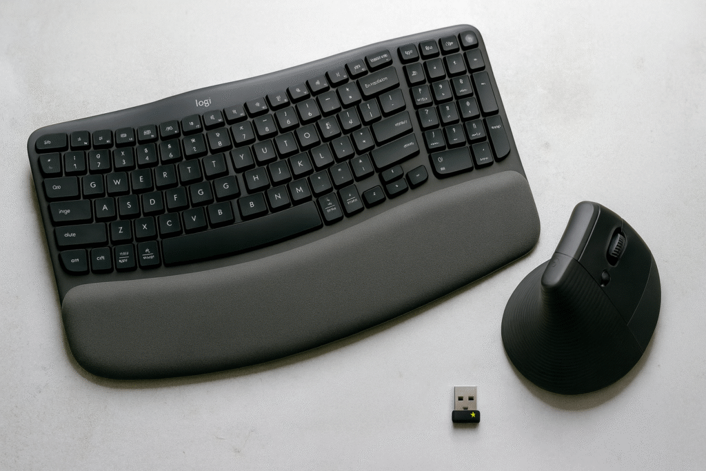 A wireless ergonomic keyboard with a cushioned wrist rest placed beside a vertical ergonomic mouse and USB receiver, photographed on a light textured surface with soft studio lighting