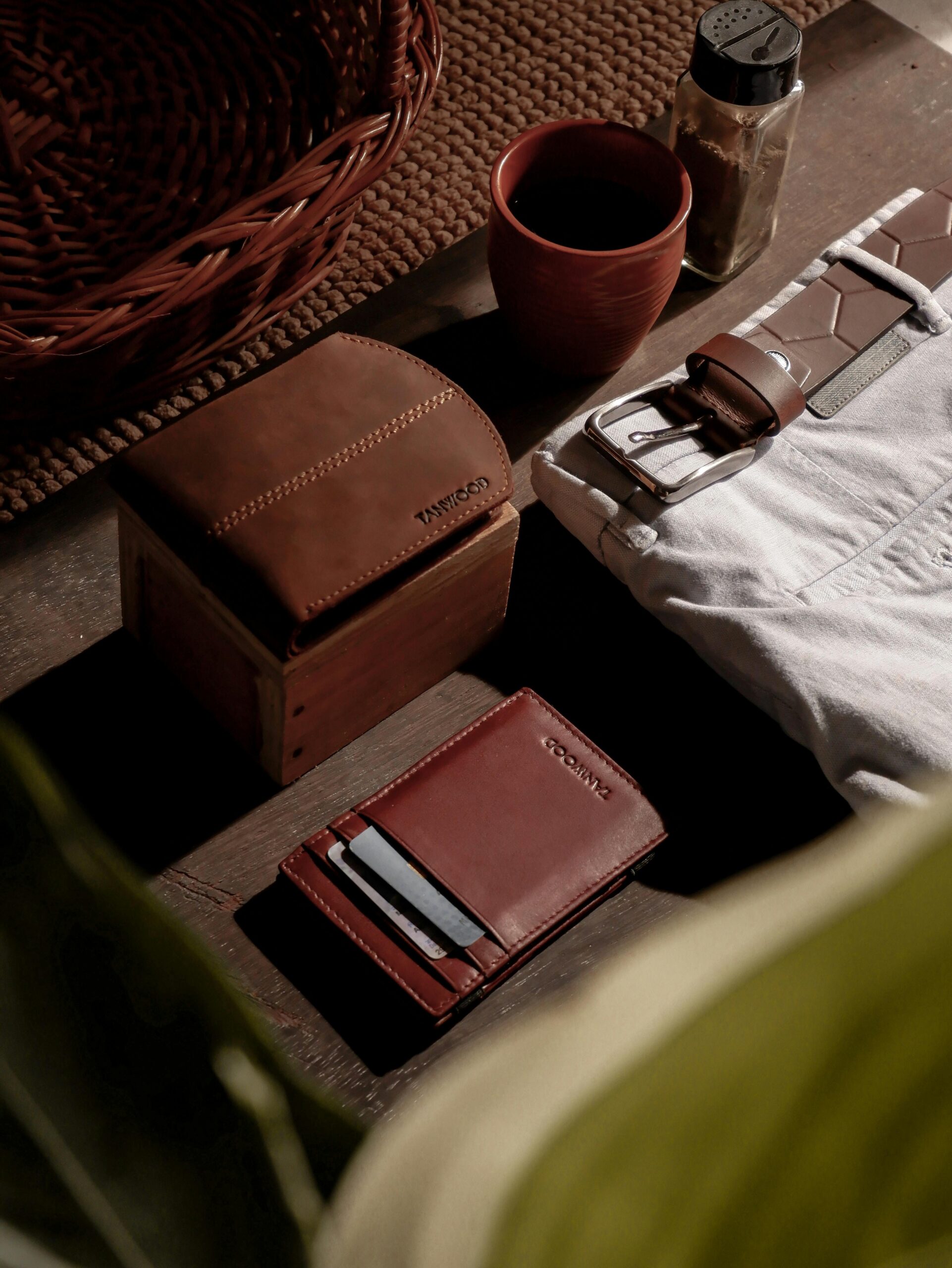 Stylish arrangement of leather wallet, belt, and other essentials on a wooden table in warm sunlight.
